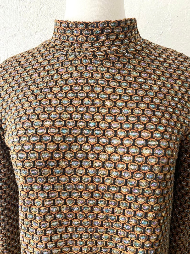May include: A black mock neck sweater with a geometric pattern in shades of brown, blue, and gold.
