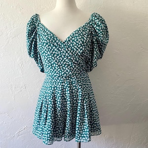 May include: A green and white floral print dress with a V-neckline and puffed sleeves. The dress has a fitted bodice and a flowy skirt.