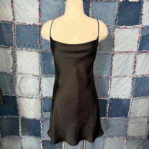 May include: A black slip dress with thin shoulder straps. The dress has a simple, elegant design and a slightly flared hemline. The dress is displayed on a mannequin against a patchwork denim background.
