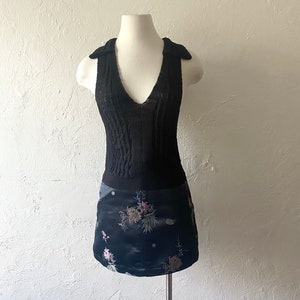 K&ouml;nnte beinhalten: Ein schwarzes &auml;rmelloses Strickoberteil mit V-Ausschnitt und einem schwarzen Rock mit Blumenmuster. Der Rock hat eine satinartige Textur.