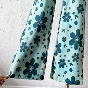 K&ouml;nnte beinhalten: Eine Hose mit weitem Bein und einem blauen und gr&uuml;nen Blumendruck. Die Hose hat ein ausgestelltes Bein und eine hohe Taille.