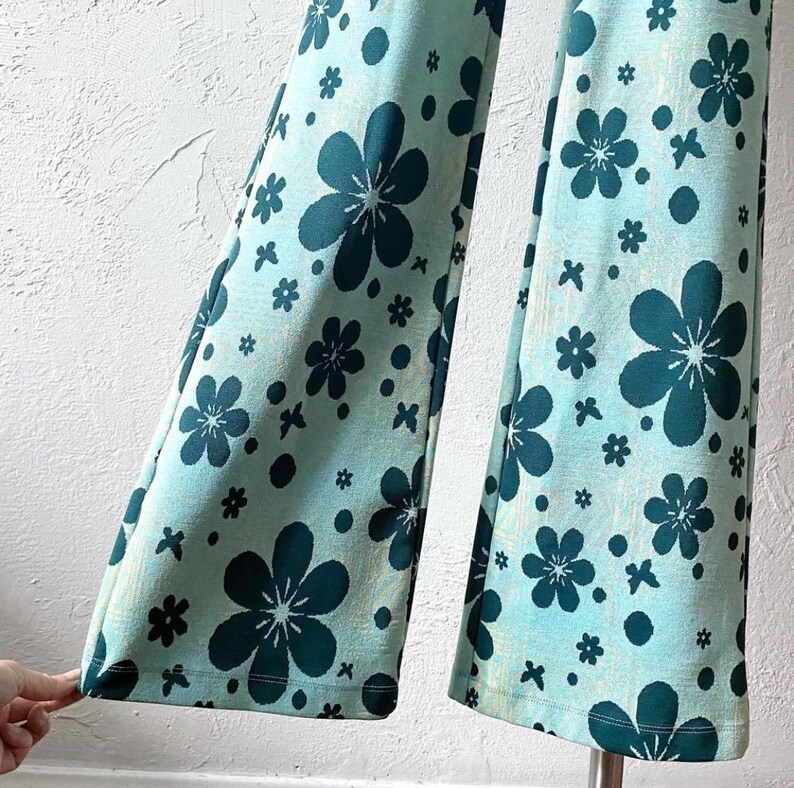 K&ouml;nnte beinhalten: Eine Hose mit weitem Bein und einem blauen und gr&uuml;nen Blumendruck. Die Hose hat ein ausgestelltes Bein und eine hohe Taille.