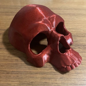 May include: A red plastic skull mask with a detailed design. The mask has eye and nose holes.