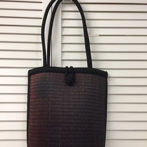 May include: A black tote bag with a woven design in shades of brown, gray, and black. The bag has two black handles and a knotted detail on the front.
