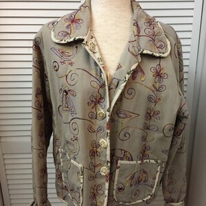 May include: A beige embroidered jacket with a floral and bird design. The jacket has a button closure and two pockets.