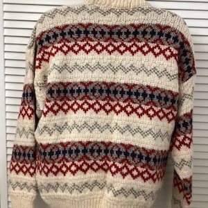 Peut inclure: Un pull en tricot crème avec un motif géométrique rouge, bleu et gris.
