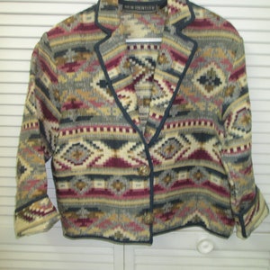 May include: A cropped, multi-colored jacket with a geometric pattern. The jacket has a navy blue trim and a single button closure. The label on the jacket reads "NEW IDENTITY".
