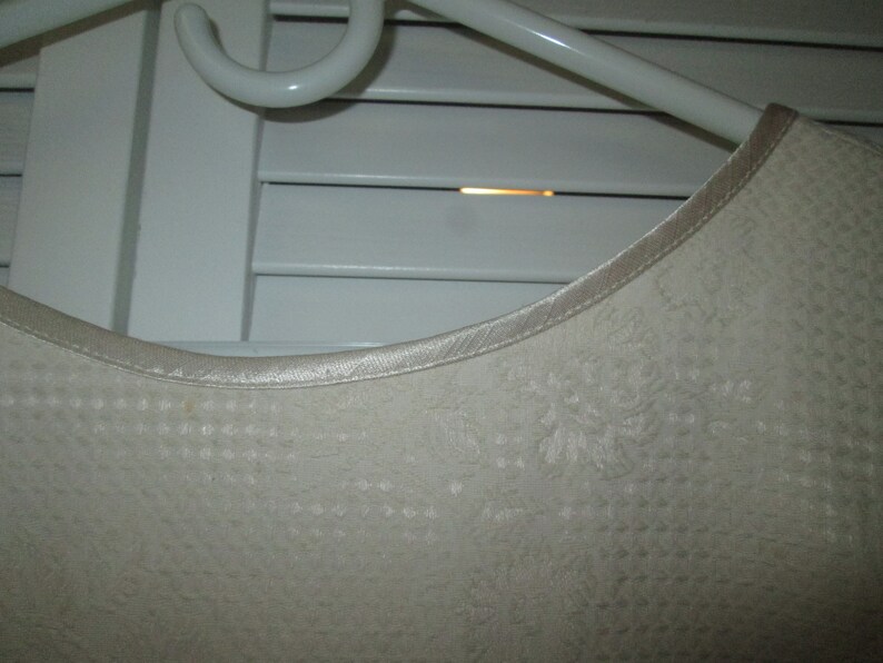 May include: A white satin-trimmed top with a delicate floral pattern. The top is made of a soft, textured fabric.