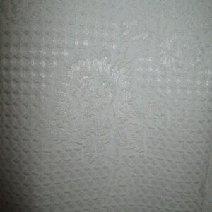May include: A close-up of a white fabric with a subtle embossed pattern. The fabric has a smooth, slightly textured surface.