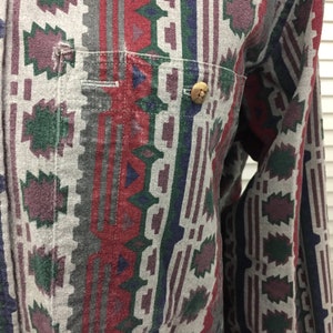 May include: A long-sleeved button-up shirt with a geometric pattern in shades of red, green, blue, and gray. The shirt has a single button on the front.