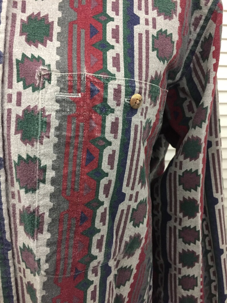 May include: A long-sleeved button-up shirt with a geometric pattern in shades of red, green, blue, and gray. The shirt has a single button on the front.