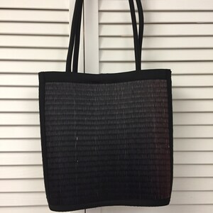 May include: A black tote bag with a woven texture and a subtle ombre effect. The bag has two black straps.