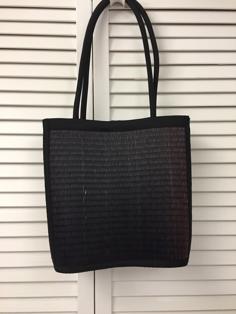May include: A black tote bag with a woven texture and a subtle ombre effect. The bag has two black straps.