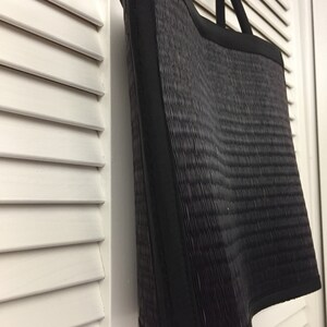 May include: Black woven tote bag with black fabric trim. The bag has a curved bottom and two black fabric handles.