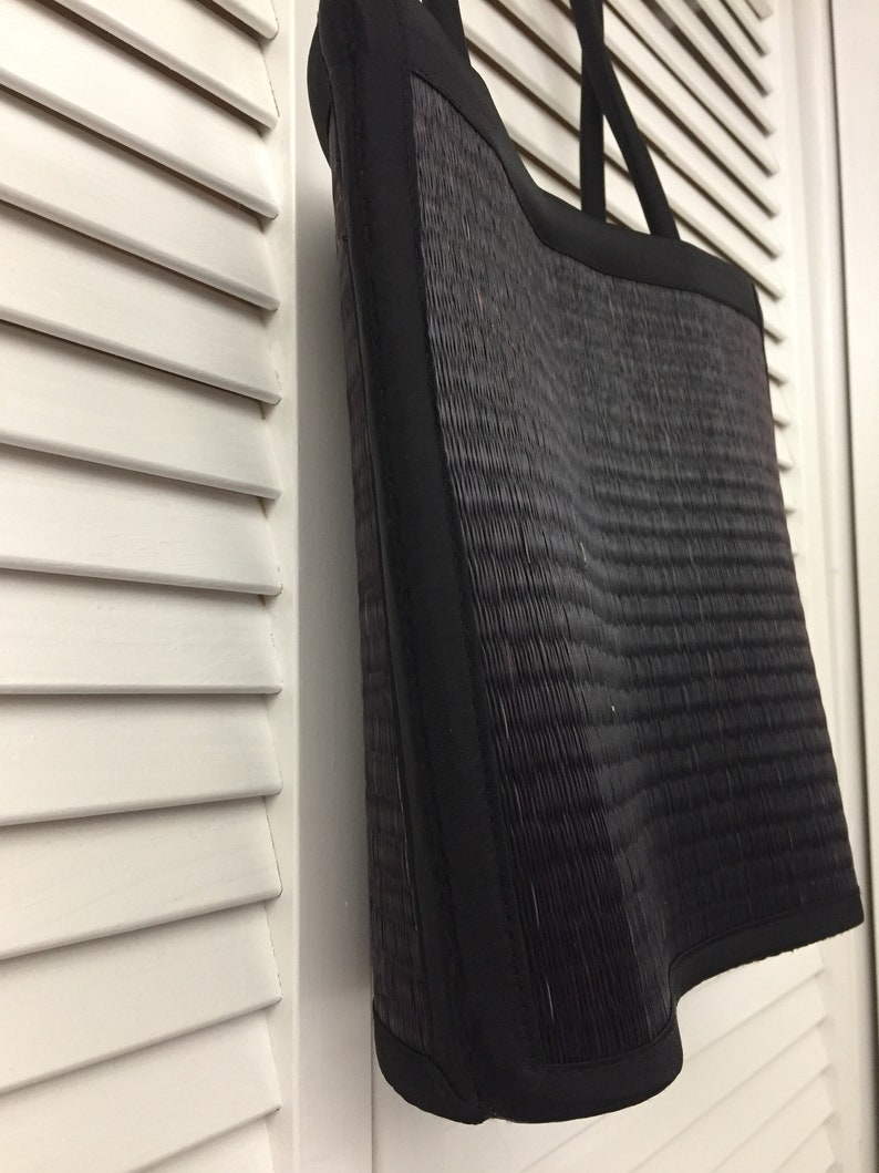 May include: Black woven tote bag with black fabric trim. The bag has a curved bottom and two black fabric handles.