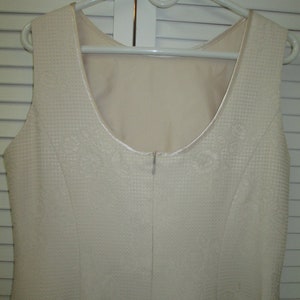 May include: A sleeveless white dress with a textured fabric and a zipper in the back.