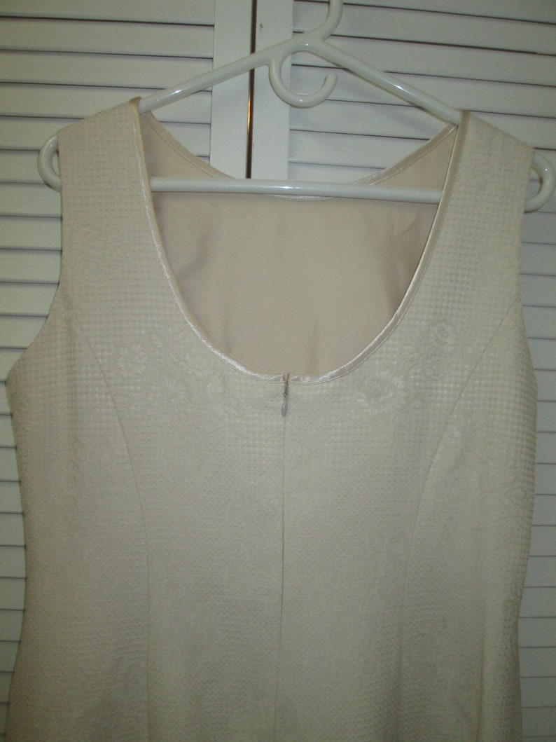May include: A sleeveless white dress with a textured fabric and a zipper in the back.