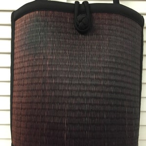 May include: A black woven tote bag with a black fabric handle and a knotted detail on the front. The bag has a gradient of colors from dark brown to black.