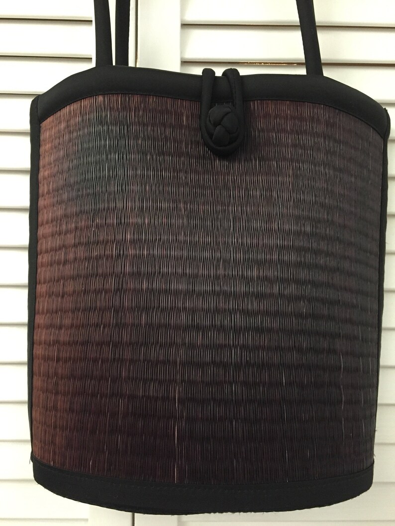 May include: A black woven tote bag with a black fabric handle and a knotted detail on the front. The bag has a gradient of colors from dark brown to black.