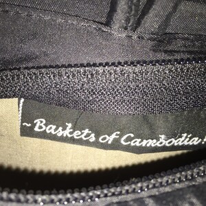 May include: Close-up of a black fabric label with white text that reads "~ Baskets of Cambodia! ~"
