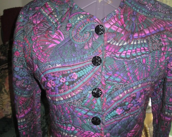 May include: A black quilted jacket with a colourful paisley pattern in shades of pink, purple, teal, and green. The jacket has a v-neck and a button closure.