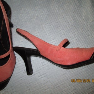 May include: A pair of coral pink suede heeled shoes with black trim and a slingback strap. The shoes have a small black heel.