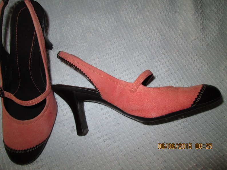 May include: A pair of coral pink suede heeled shoes with black trim and a slingback strap. The shoes have a small black heel.
