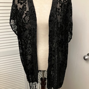 May include: Black sheer lace kimono with a floral pattern and fringe trim.