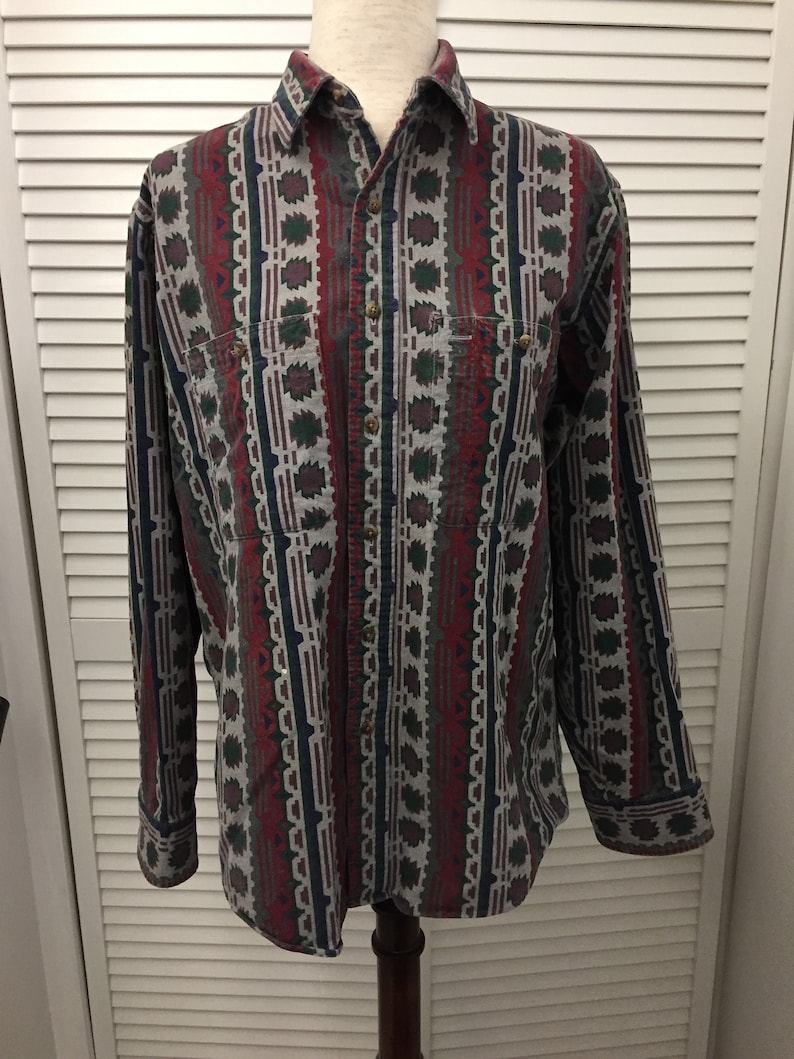 May include: A long-sleeved button-down shirt with a geometric pattern in shades of red, green, blue, and gray. The shirt has a pointed collar and a button-up front. The sleeves have button cuffs.