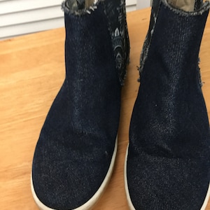 Peut inclure: Une paire de bottines en jean bleu foncé avec des semelles blanches. Les bottes ont un aspect vieilli et sont faites d'un matériau doux et confortable.