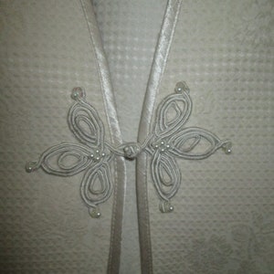 May include: A white garment with a decorative knot closure featuring a series of loops and white beads.