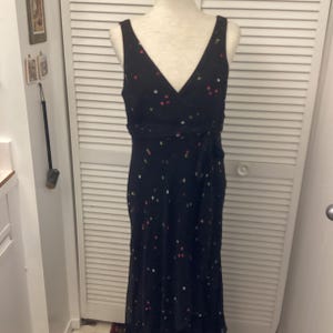 May include: A sleeveless black dress with a V-neck and a wrap-style waist. The dress is adorned with small, colorful polka dots in pink, white, and green. The dress is displayed on a mannequin.