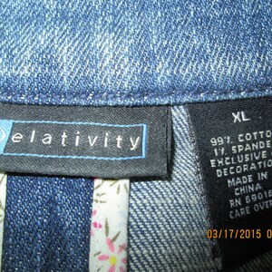 May include: A black and white label with the text "(r)elativity" and a size tag that says "XL". The tag also includes the fabric composition: 99% cotton and 1% spandex. It states that the decoration is exclusive of the fabric and that the item was made in China. The tag also includes the RN number 59016 and a care over instruction. The date 03/17/2015 04:43 is printed on the tag.