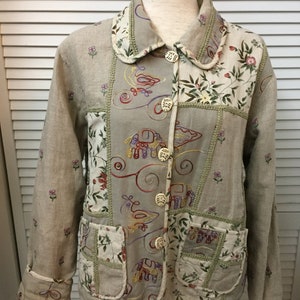 May include: A beige linen jacket with a patchwork design featuring embroidered birds, elephants, and floral patterns. The jacket has a collared neckline, long sleeves, and button closures.