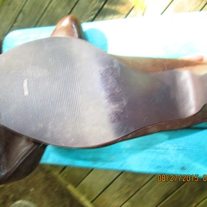 May include: Close-up of the bottom of a brown leather boot with a textured rubber sole. The sole has a slight wear pattern.