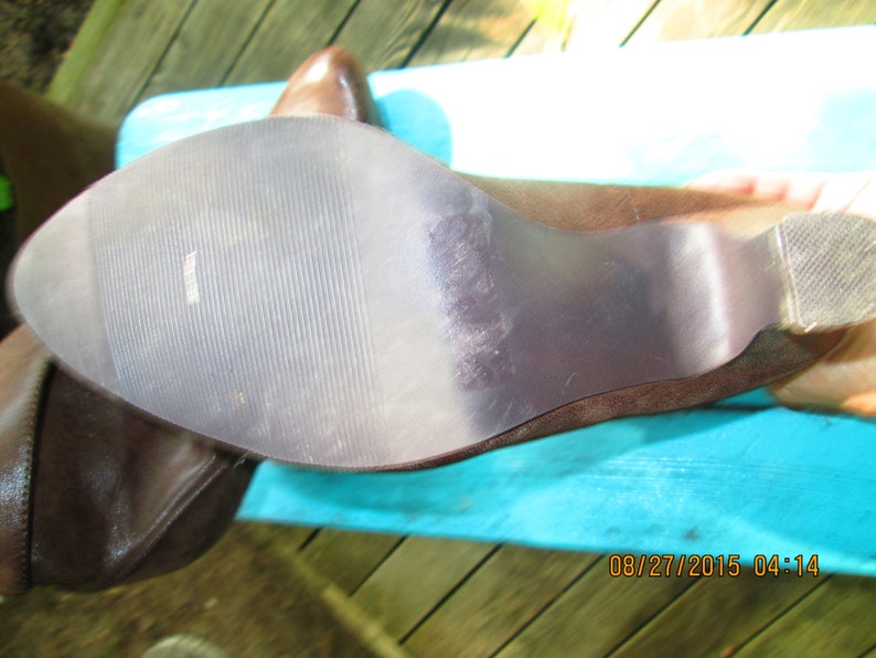 May include: Close-up of the bottom of a brown leather boot with a textured rubber sole. The sole has a slight wear pattern.