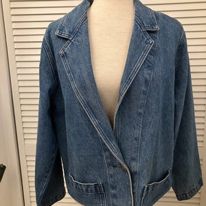 Peut inclure: Une veste en jean bleu avec une fermeture à bouton unique et un col pointu. La veste a deux poches sur le devant et une longueur écourtée.