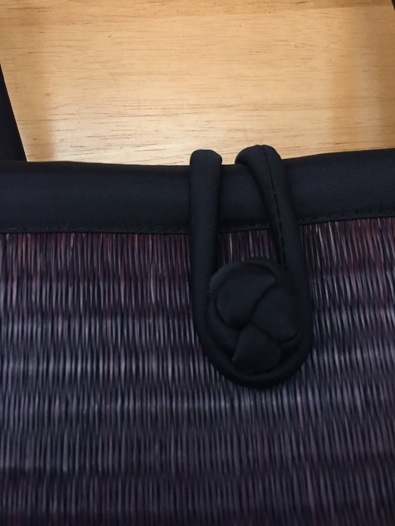 May include: A black woven bag with a black fabric handle. The handle has a knotted detail.