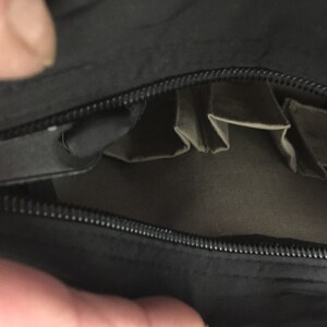 May include: A black zippered pouch with multiple interior pockets. The pouch is open and the pockets are visible.