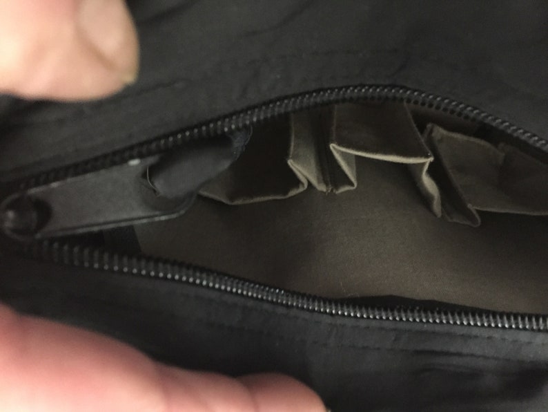 May include: A black zippered pouch with multiple interior pockets. The pouch is open and the pockets are visible.