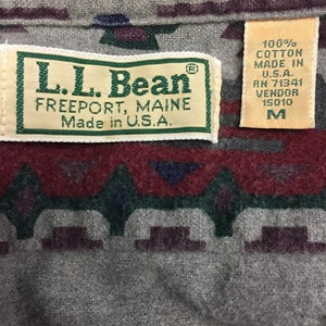 May include: A brown, green, and red patterned flannel shirt with a L.L. Bean label. The label says "L.L. Bean, Freeport, Maine, Made in U.S.A." and has a size tag that says "M".
