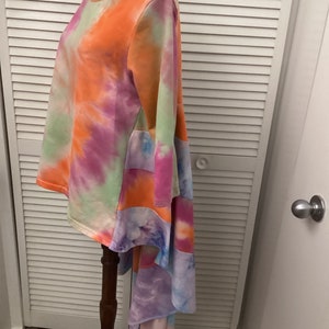 May include: A tie-dye long-sleeved shirt with a high-low hemline. The shirt is made of a soft, comfortable fabric and features a unique patchwork design with a mix of orange, pink, green, and blue colors.