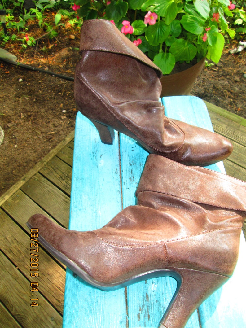 May include: A pair of brown leather heeled boots with a folded-over cuff. The boots are on a blue wooden surface.