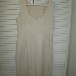 May include: A sleeveless white dress with a subtle pattern. The dress has a scoop neckline and a zipper closure in the back.