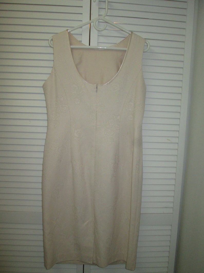 May include: A sleeveless white dress with a subtle pattern. The dress has a scoop neckline and a zipper closure in the back.