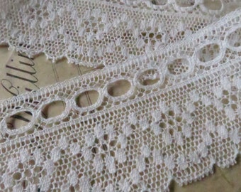 May include: White lace trim with a scalloped edge and a repeating pattern of small circles and larger ovals. The lace is delicate and intricate.