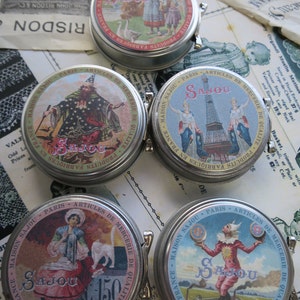 May include: Four vintage metal tins with lids, each featuring a different colorful illustration and the text "Maison Sajou Paris - Articles de Mercerie de Qualite - Produits Fabriques en France".