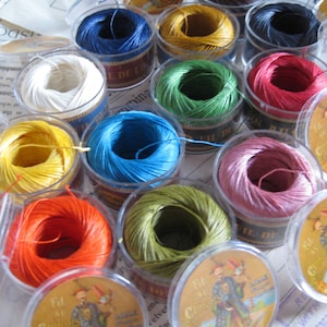 Pode incluir: Conjunto de carretéis de fio em várias cores, incluindo branco, amarelo, laranja, vermelho, verde, azul e castanho. Os carretéis estão em recipientes de plástico transparente com etiquetas que dizem "Fil Au Chinois" e "Fit Au Chinois".