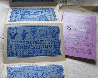 Puede incluir: Un folleto de patrones de punto de cruz vintage con un diseño azul y blanco. La portada presenta el texto "S: Ялочи" y "ALBUMS". El folleto incluye patrones para alfabetos, animales y un diseño que dice "Buen provecho".