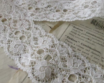 May include: White lace trim with a delicate floral pattern and small holes. The lace is approximately 1 inch wide.